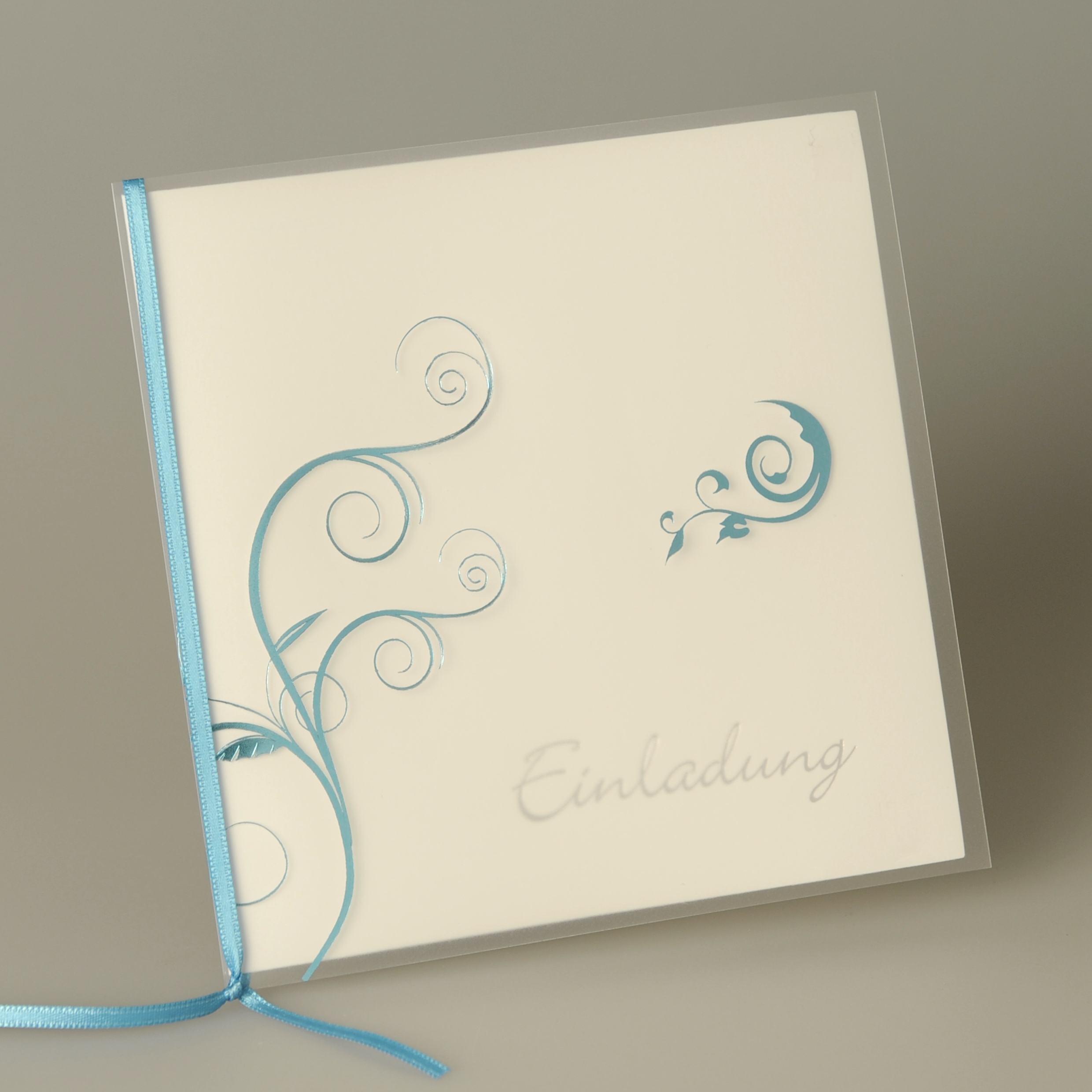 Weiße quadratische Karte mit Kunststoffumschlag, türkisfarbenem Band und weißem Kuvert.