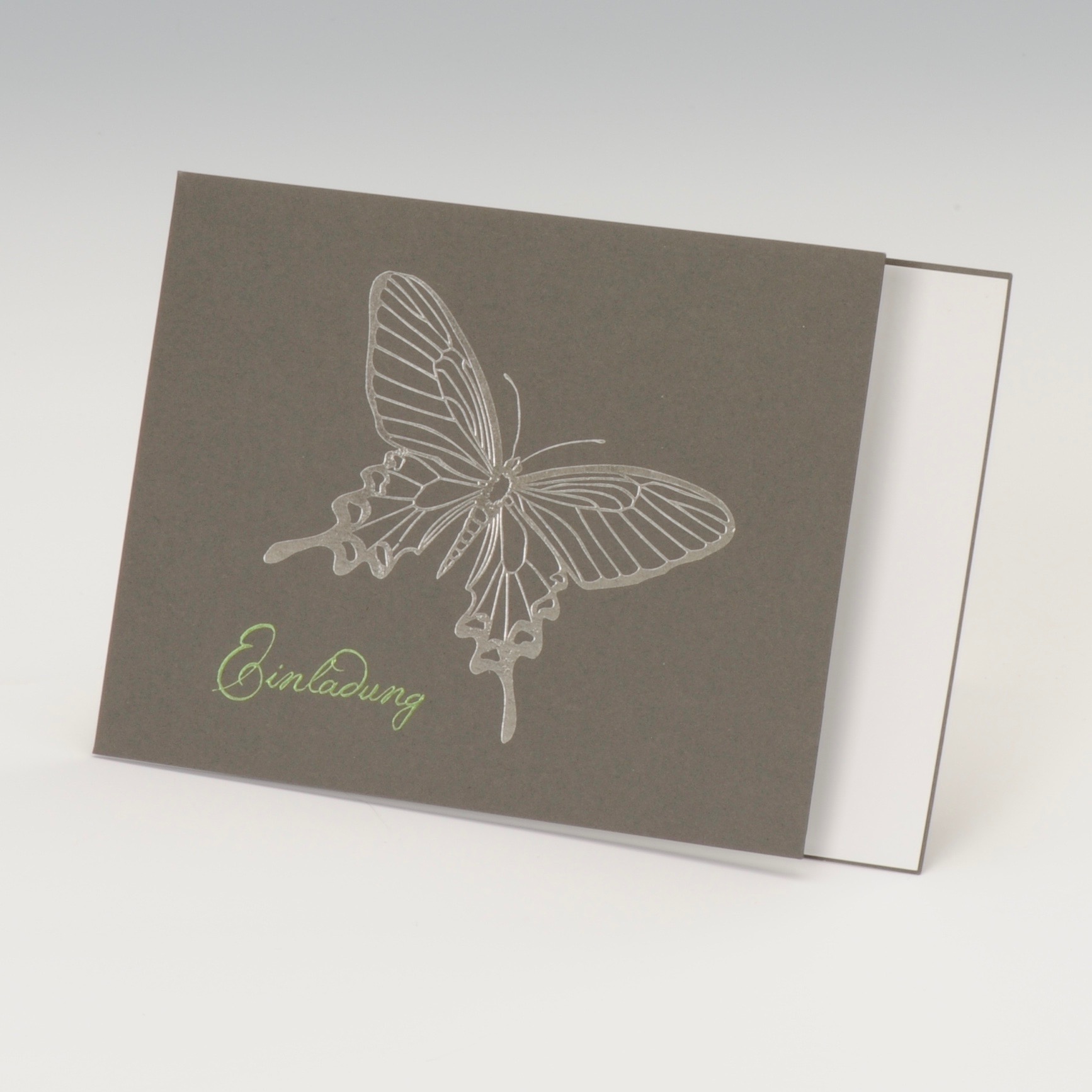 Graue Karte mit silber geprägtem Schmetterling auf der Vorderseite, Einleger weiß, Kuvert grün.